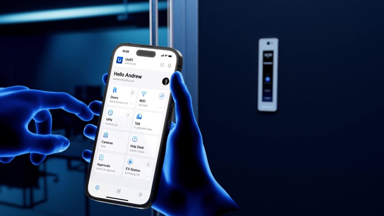 Hand holding a phone running an access control app beside a door-mounted reader